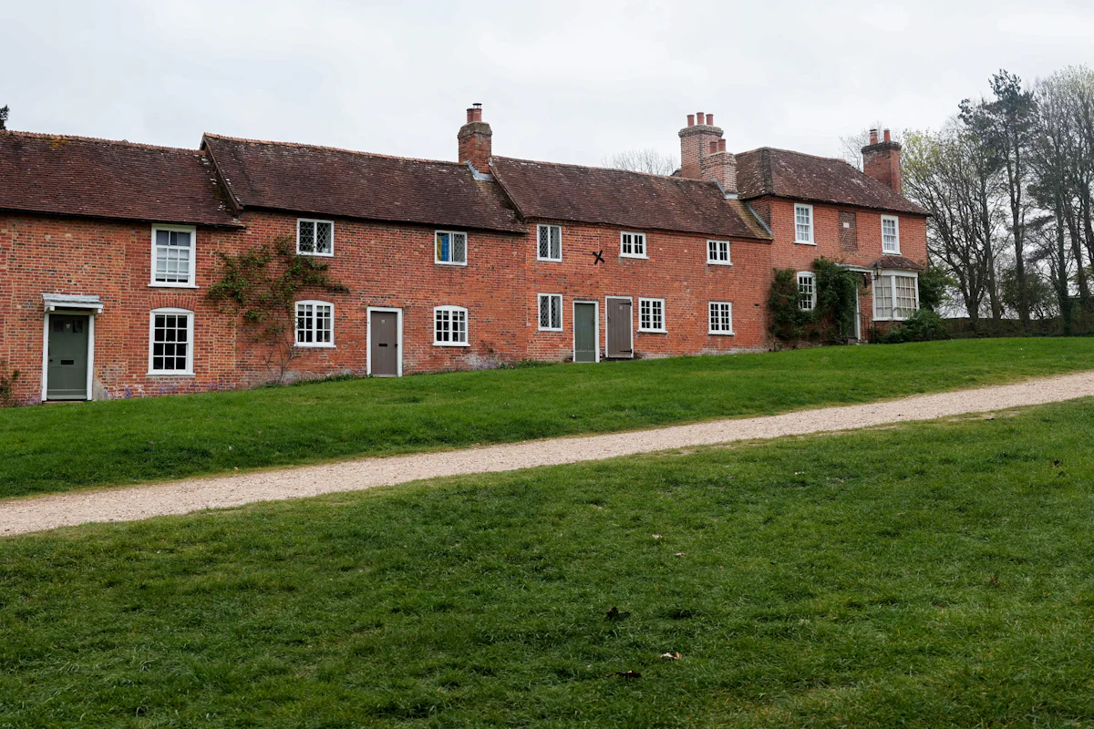 A terrace of red brick cottages with white windows and green doors, set back behind a green